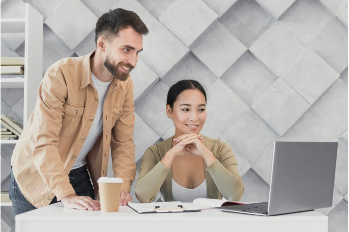 A man and woman working on a laptop at an office table.